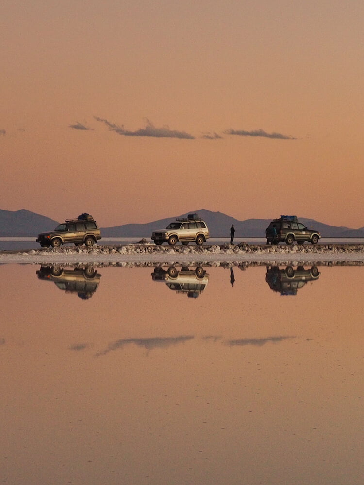 Three cars parked in a line are perfectly reflected in a lake beneath them