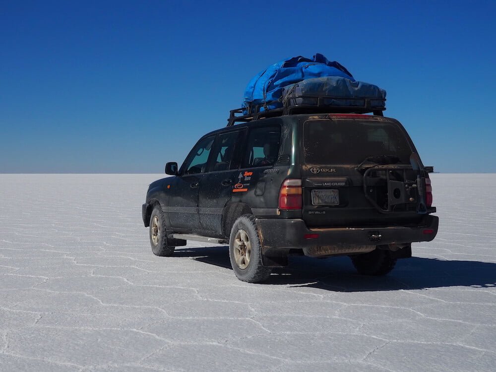 Uyuni Salt Flats of Bolivia - our jeep. A jeep is parked on a flat white salt flat with blue sky above