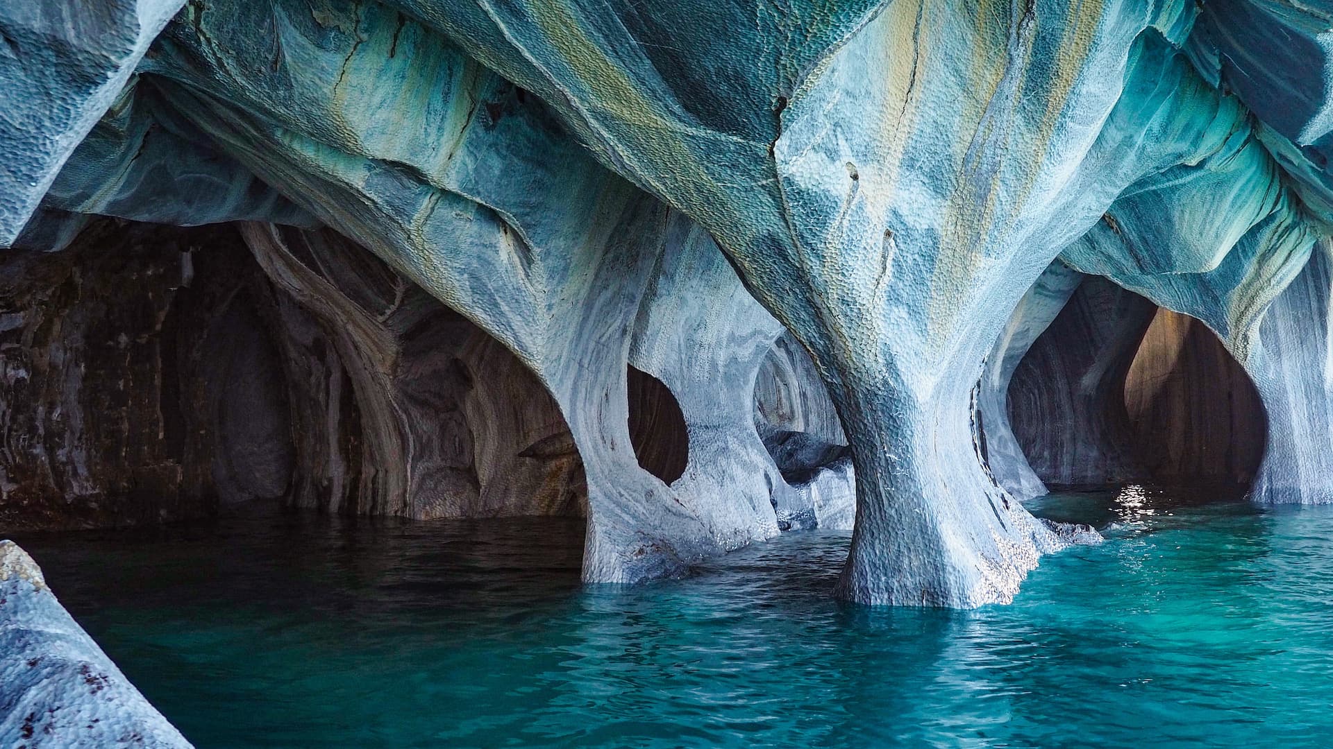 Inside of a cave with marble-coloured rocks and turquoise water below