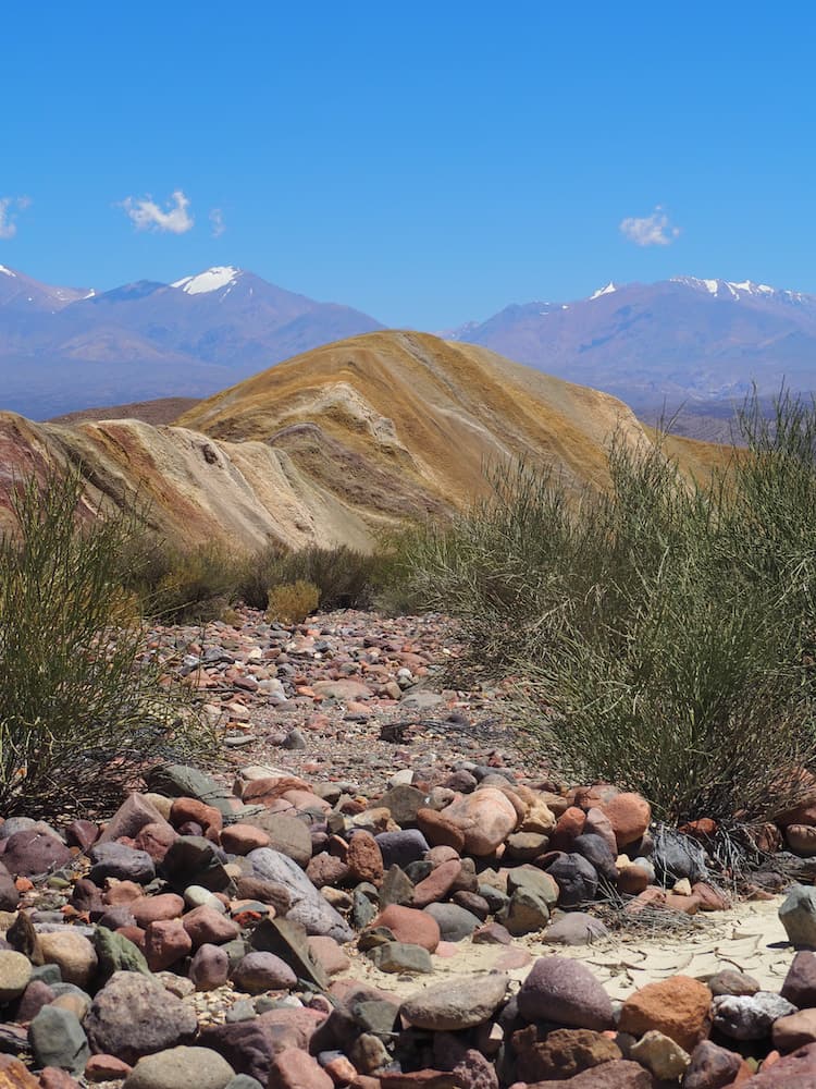 Boulders in the foreground, multi-coloured hills in the middle ground, snow-capped mountains in the background