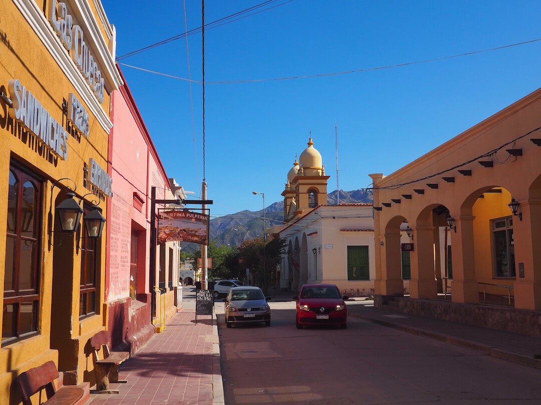 A street with yellow and pink buildings and a church in the background
