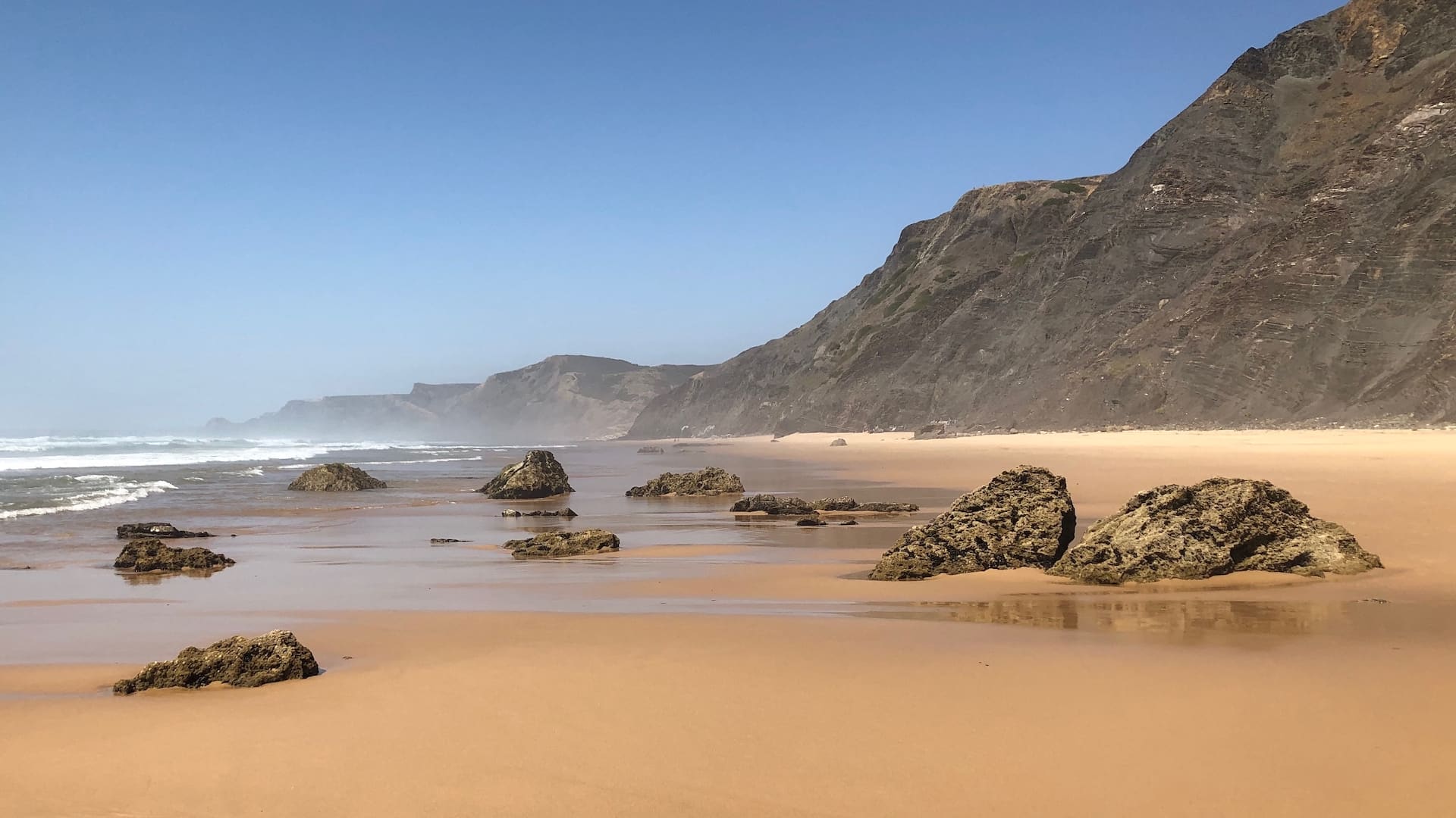 An empty beach with cliffs at the rear and rocks embedded in the sand