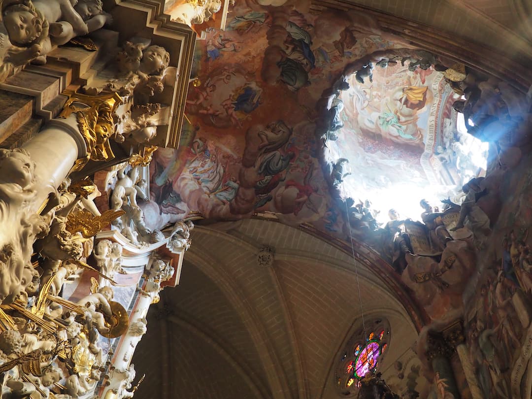 A ceiling fresco painting is illuminated by light shining through a dome above