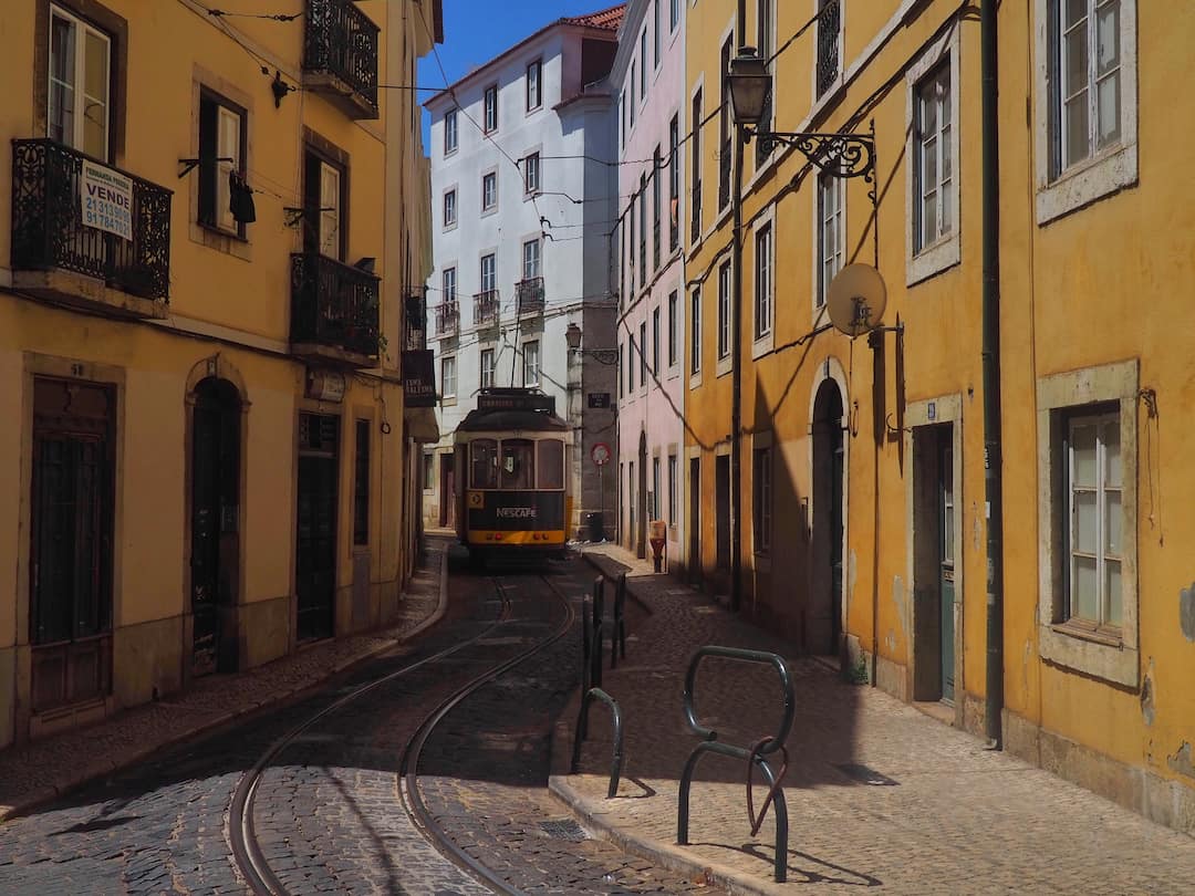 A tram approaches within a narrow street of yellow buildings