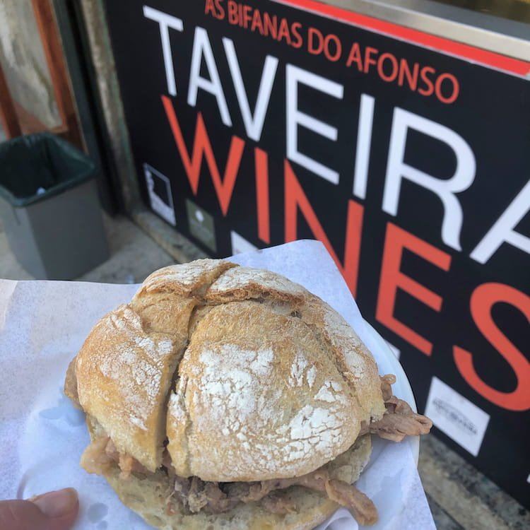 A meat-filled bread roll held in front of a snack bar sign