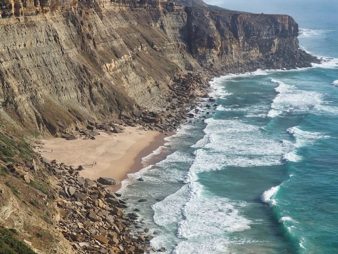 Tall cliffs on the left drop to a small golden beach and the sea