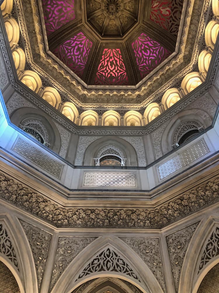 Internal view of a purple coloured dome ceiling leading down to a silver and gold wall with intricate carvings