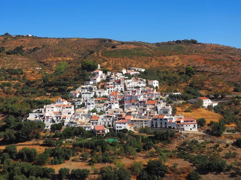 A triangular-shaped village of whitewashed buildings and red roofs clings to a mountainside