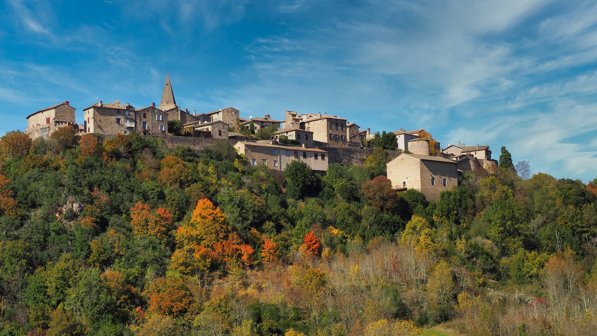 An old stone-built town looks out over a hillside of autumnal trees