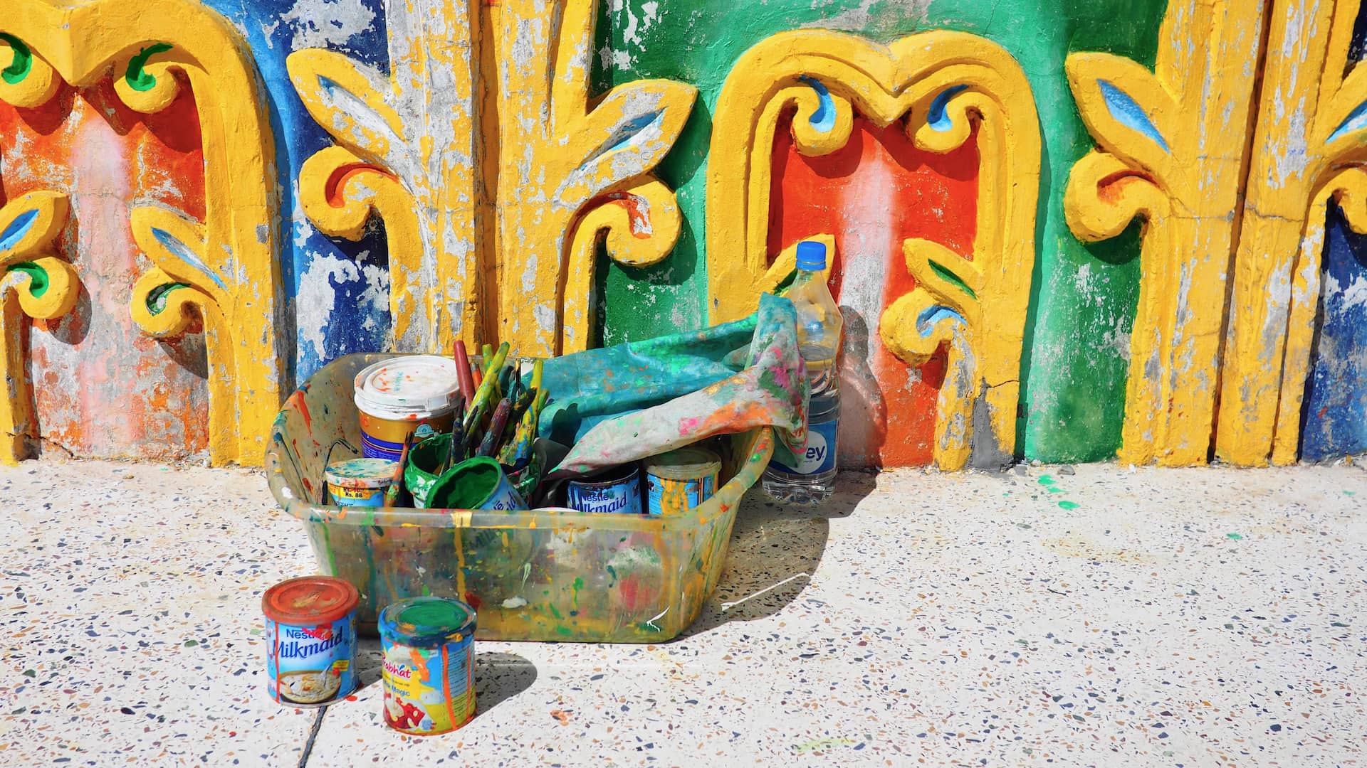 Pots of paint in front of a building wall coloured red, blue, green and yellow