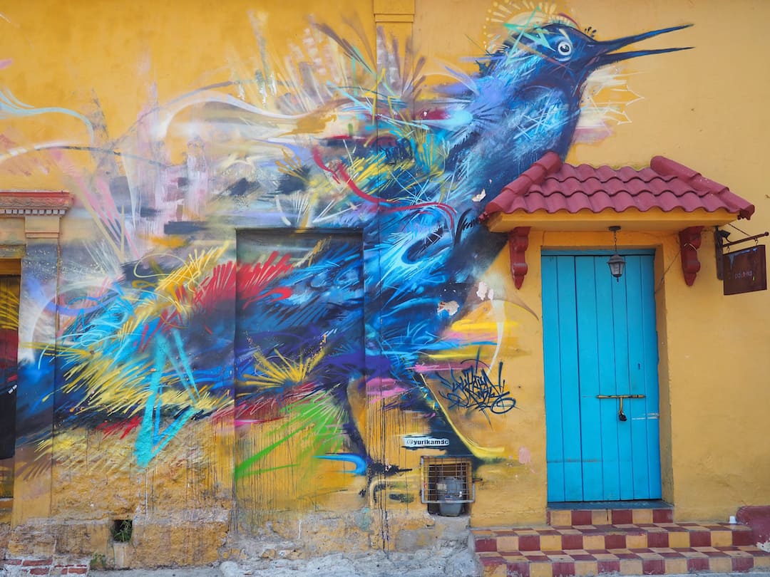 A painting of a blue bird on a yellow wall