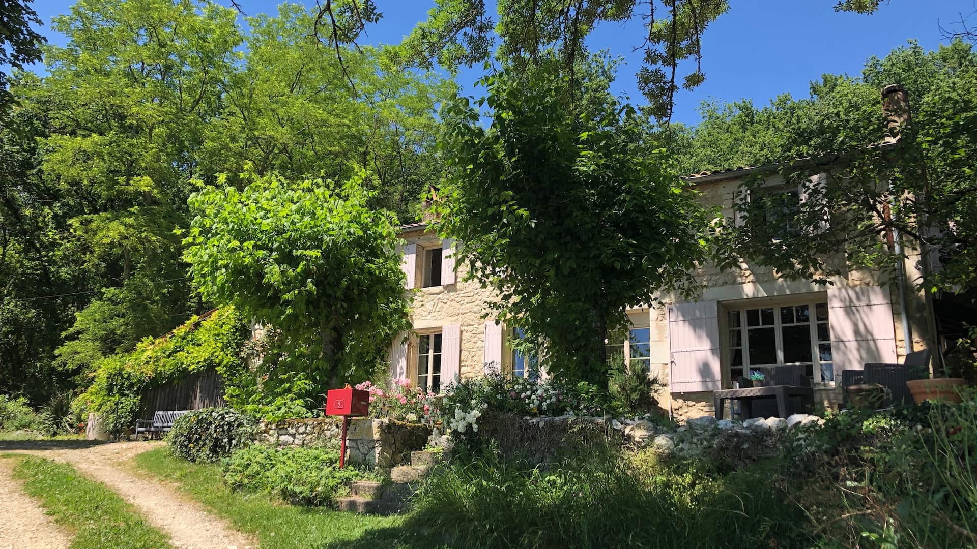 A stone farmhouse surrounded by trees and a red post box