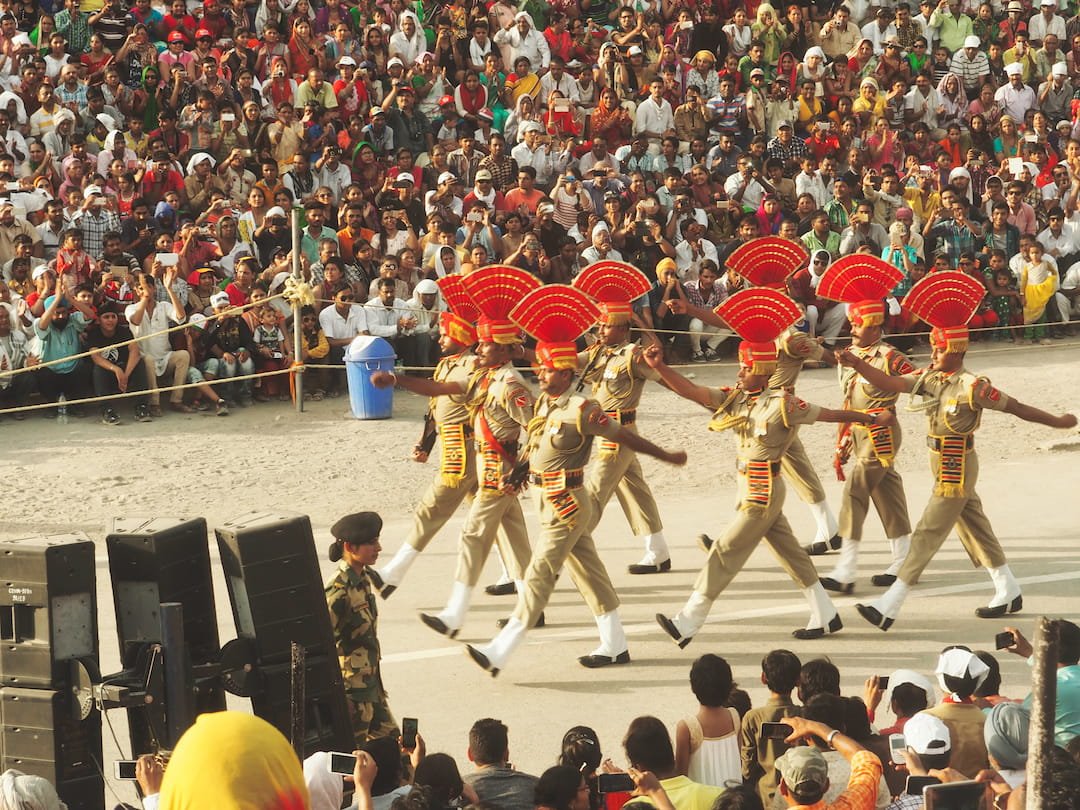 Eight soldiers in three rows march in front of a seated crowd