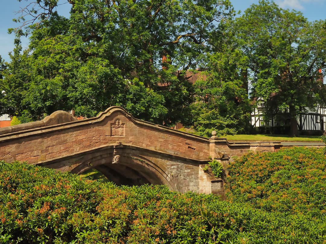 Sandstone bridge surrounded by trees with half-timbered black and white buildings in the background