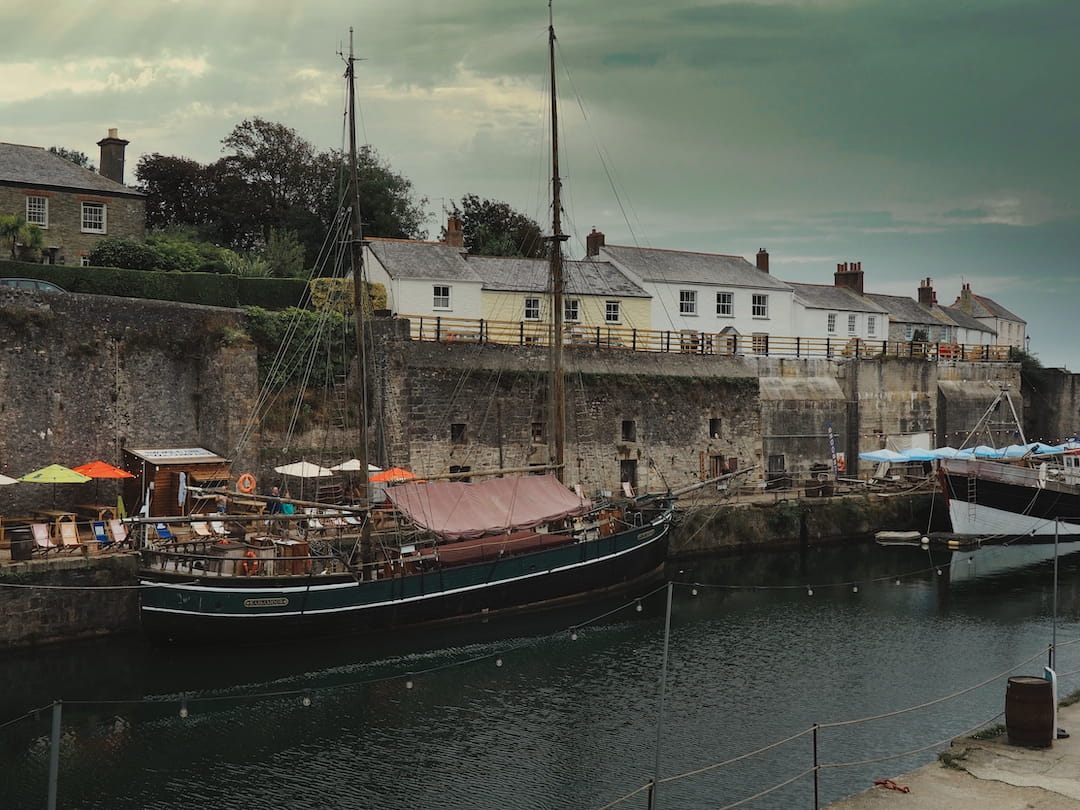 A wooden boat in a harbour in front of a stone wall with houses behind
