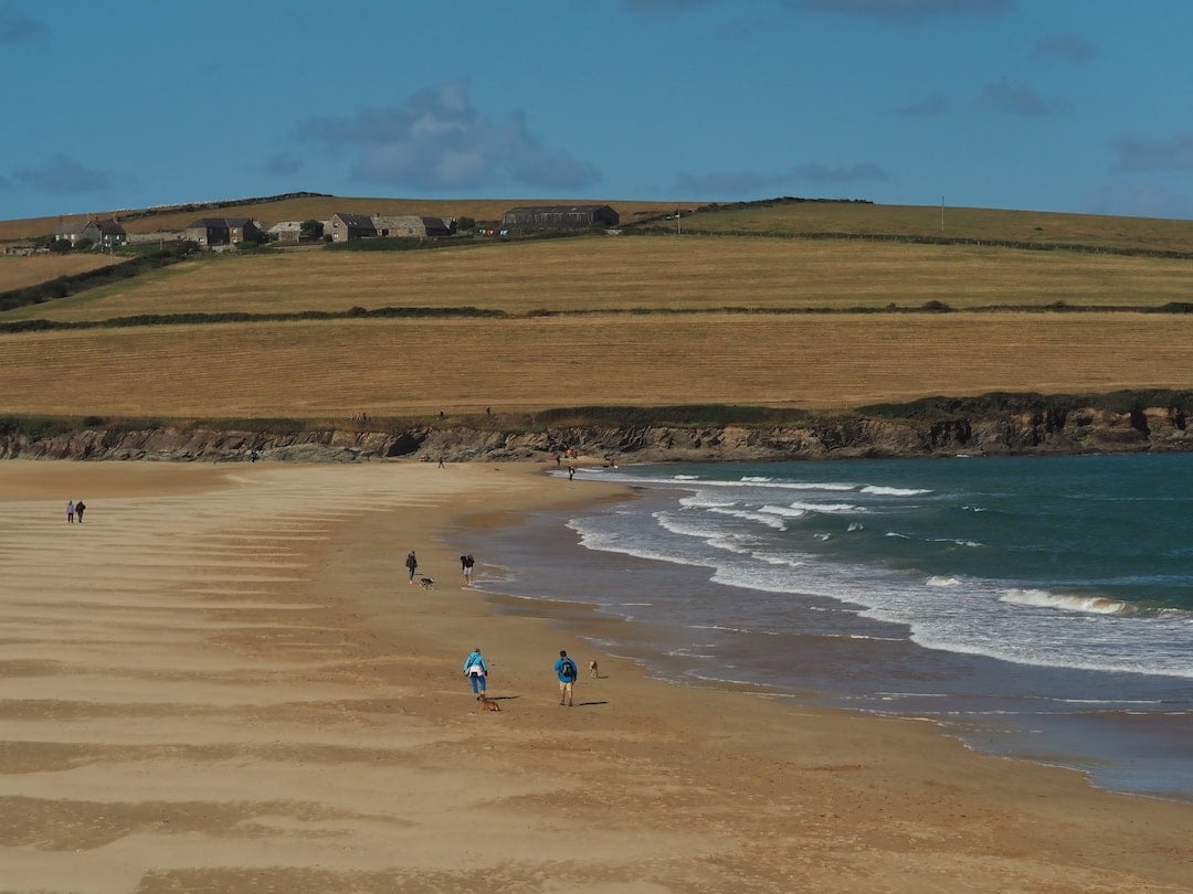 A wide sandy beach to the left with hilly farmland in the background