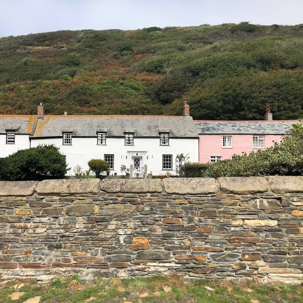 A stone wall in the foreground with pink and white coloured cottages in the background