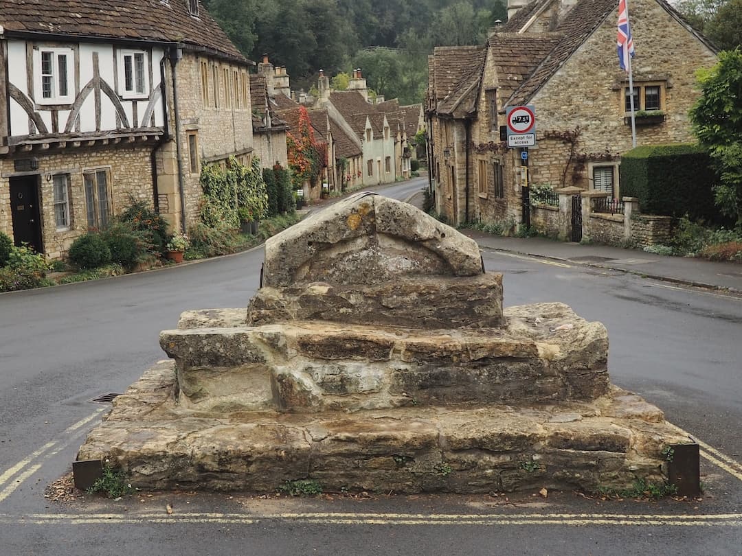 A stone structure in the middle of the road leading off to a street of cottages