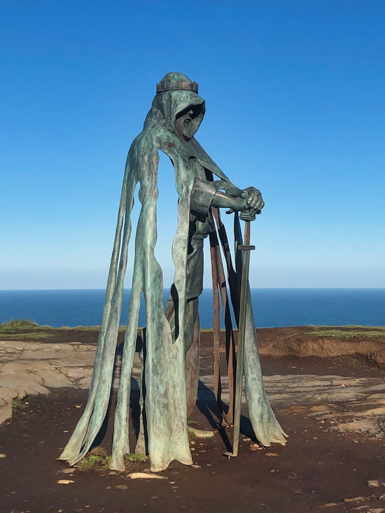 A statue of a man holding a sword on a clifftop with the sea in the background