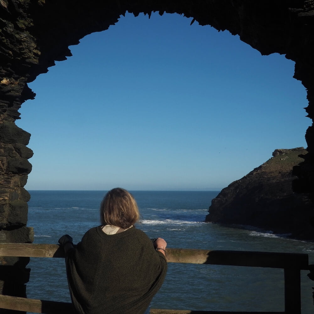 A woman looks out to sea through a natural window in a stone wall