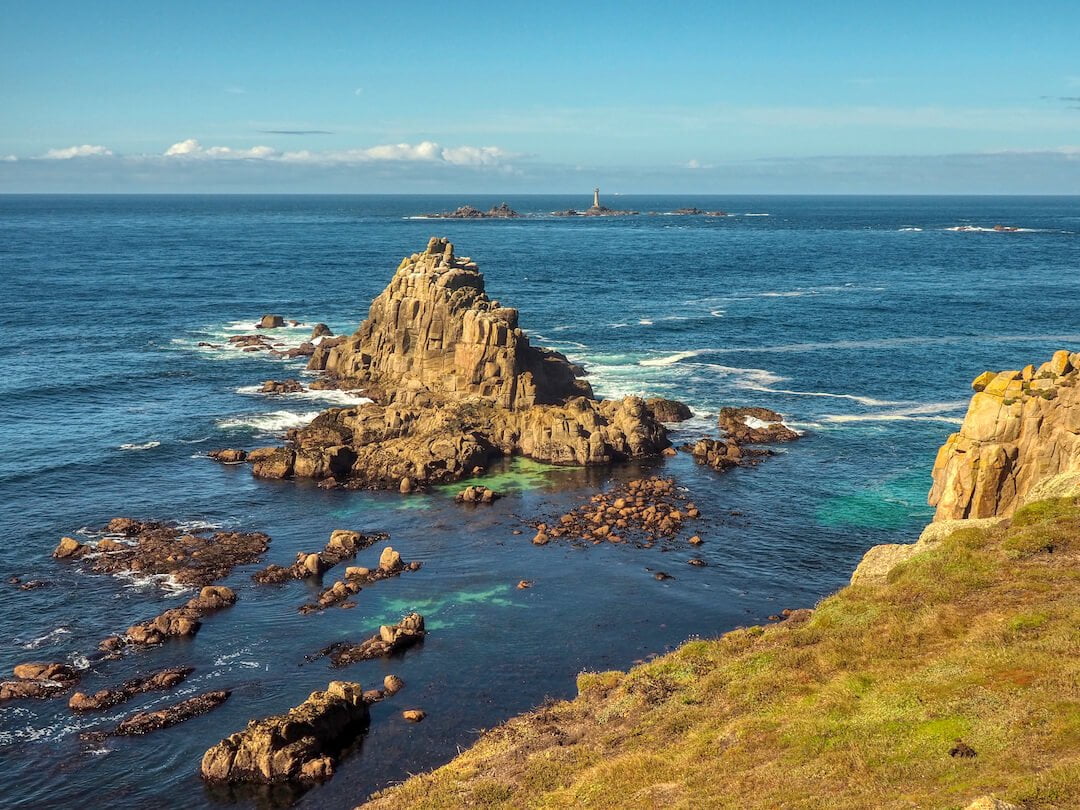 An offshore rocky outcrop in the foreground and a lighthouse in the background