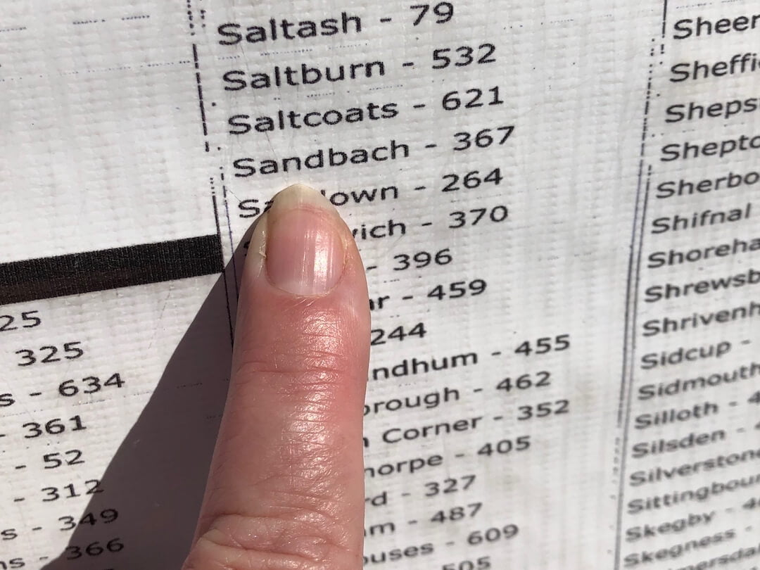 A finger points to a list of place names on a white background