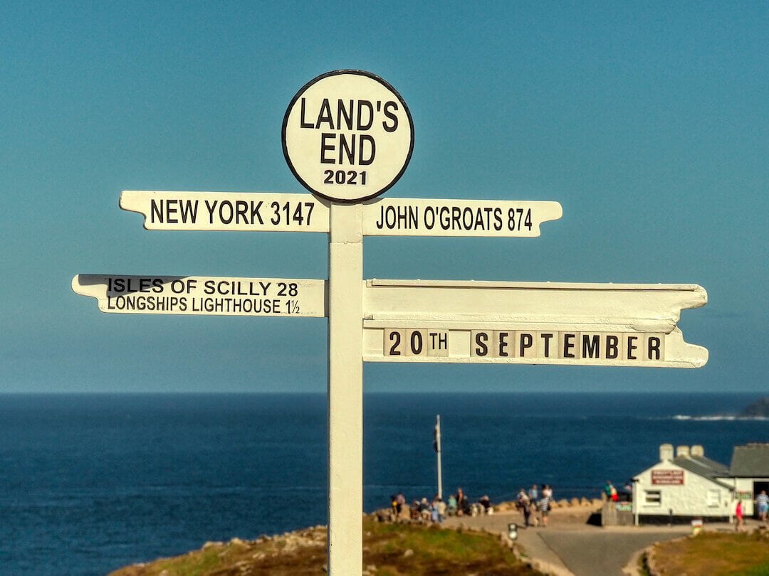 A white road sign shows distances in miles to various destinations with the sea as a background