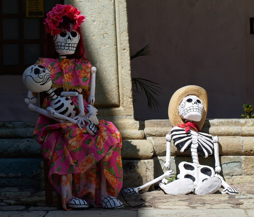 A skeletal mother is seated holding a skeleton of a child, while a skeletal father sits on the ground beside her