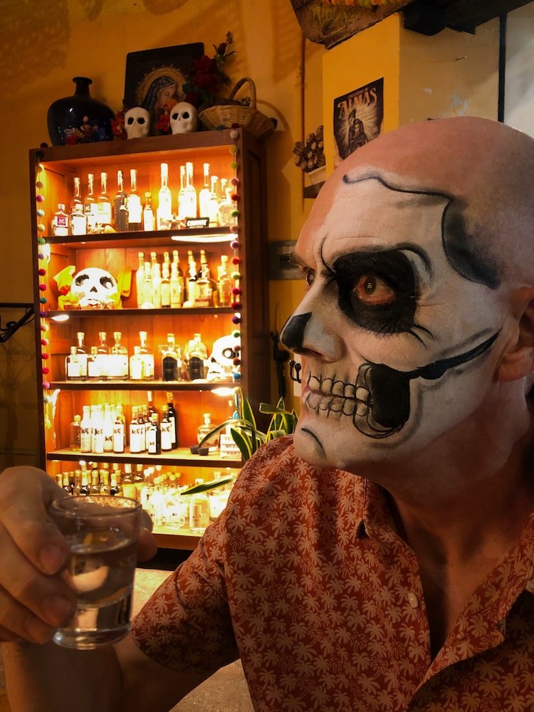 Ian in face paint drinks a mezcal in a bar