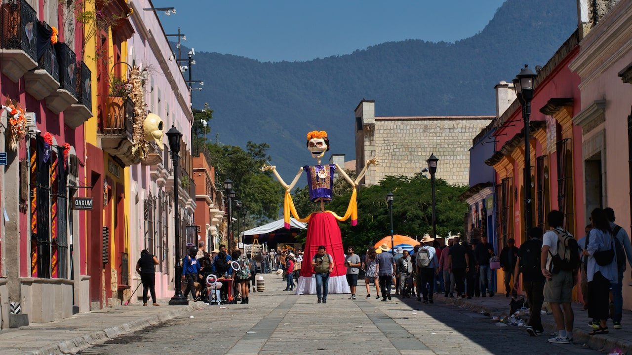 A giant puppet stands with arms raised in a Oaxaca street