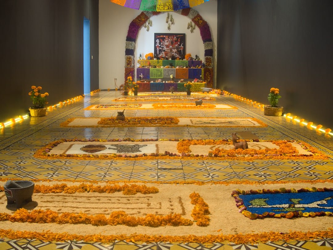 A public ofrenda with lots of sand art and magnolias laid out in front of it
