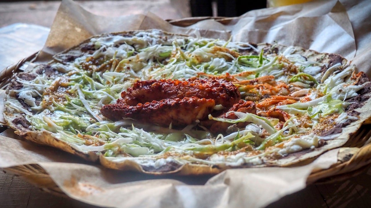 A thin giant tortilla is smothered with refried beans, cabbage and avocado and topped with grilled octopus